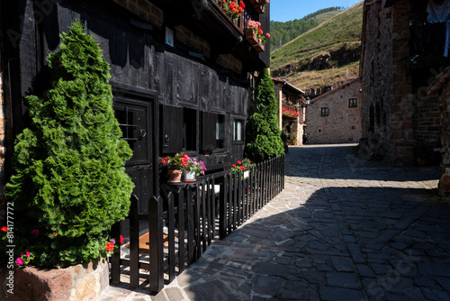 Small medieval village with cobblestone streets and a stone building with a black fence with potted colorful flowers, Barcena Mayor, Saja-Besaya Natural Park, Cantabria, Spain.