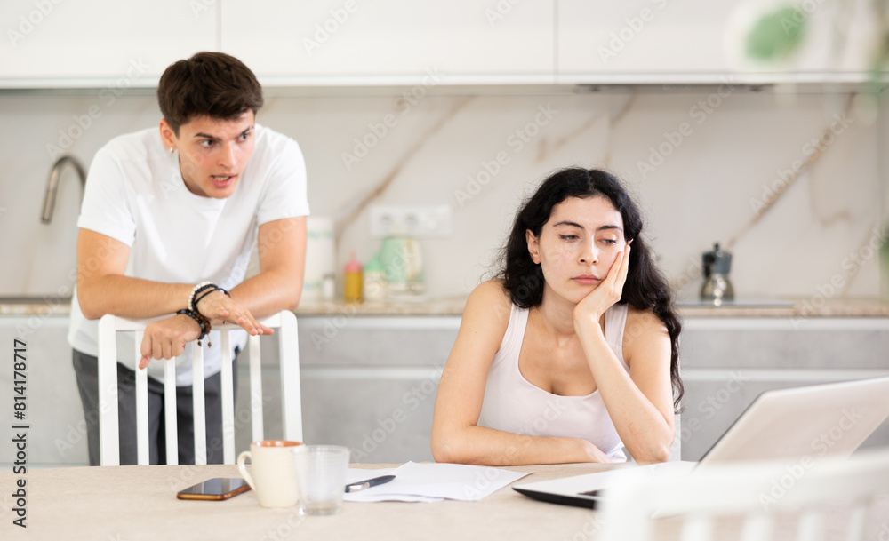 Obraz premium Young guy screams during family quarrel with young woman using laptop in kitchen