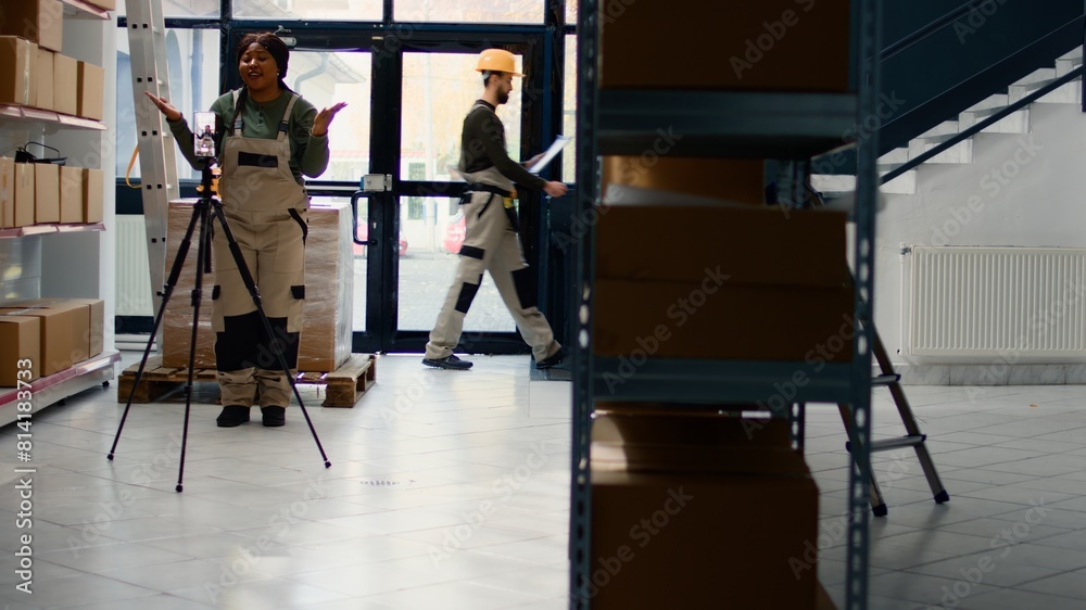 Warehouse marketing executive using smartphone placed on tripod to make video for social media platforms. African american advertising specialist films herself in storage hub showcasing her business Warehouse marketing executive using smartphone placed on tripod to make video for social media platforms. African american advertising specialist films herself in storage hub showcasing her business