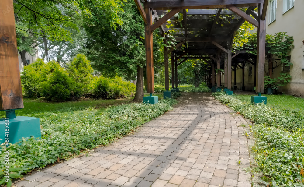 Altana - pergola w parku. Chodnik wśród obfitości letniej roślinności. Parkowe maleńkie alejki – wybrukowane i biegnące pośród pięknie obsadzonych roślin wśród architektury ogrodowej.