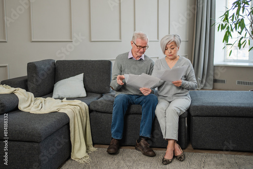 Sad tired disappointed middle aged senior couple sit with paper document. Unhappy older mature man woman reading paper bill managing bank finances calculating taxes planning loan debt pension payment © Юлия Завалишина