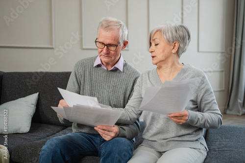 Sad tired disappointed middle aged senior couple sit with paper document. Unhappy older mature man woman reading paper bill managing bank finances calculating taxes planning loan debt pension payment