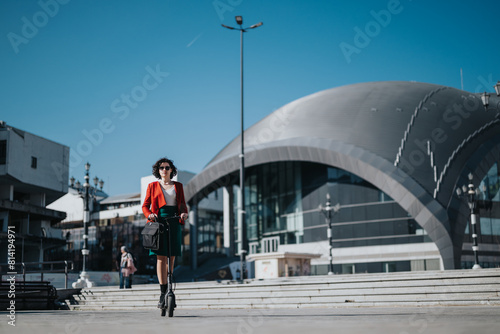 A professional businesswoman in stylish attire riding electric scooter confidently outside an urban building on a sunny day.