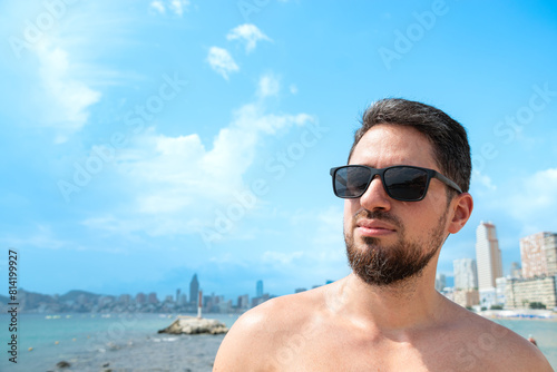 Young Hispanic man model smiling with sunglasses on beach posing sideways