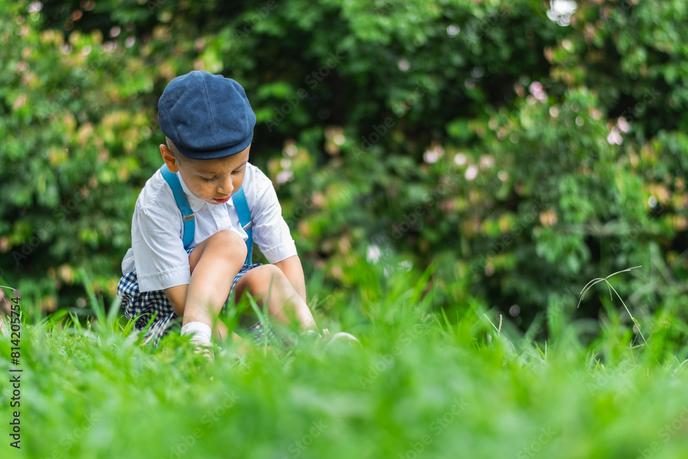 little latino boy sitting on the grass looking down at the ground, wearing a beret and white shirt little latino boy sitting on the grass looking down at the ground, wearing a beret and white shirt