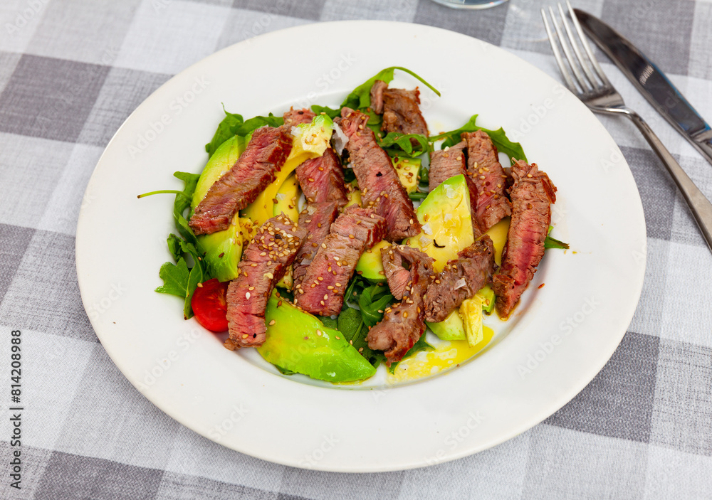 Delicious grilled beef served with avocado and herbs on plate