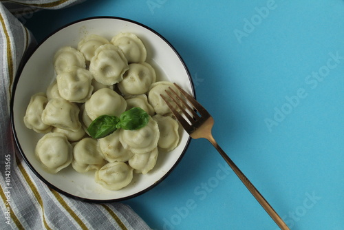 Table setting dumplings in a bowl with fork, napkin and herbs basil top view on a blue background with space for text copyspace