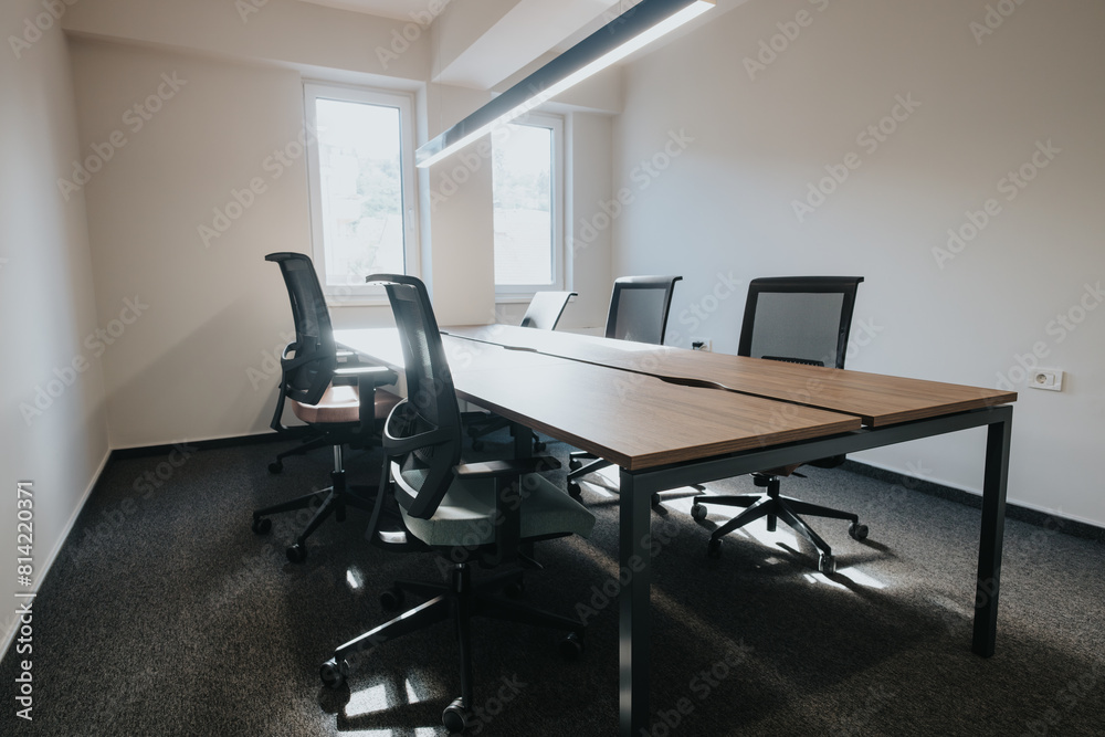 Contemporary office space featuring a stylish wooden conference table, ergonomic chairs, and a well-lit, clean environment ideal for business settings.