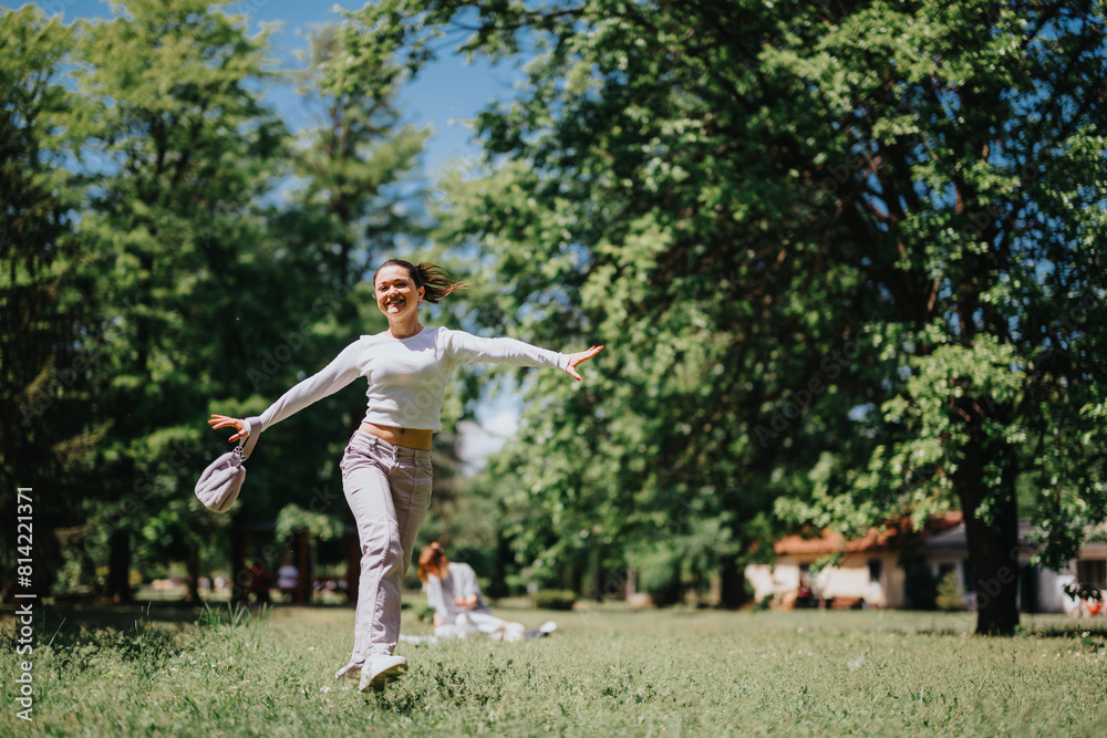 A happy young woman spreads her arms wide as she walks carefree through a sunny, green park, embodying joy and freedom. A happy young woman spreads her arms wide as she walks carefree through a sunny, green park, embodying joy and freedom.