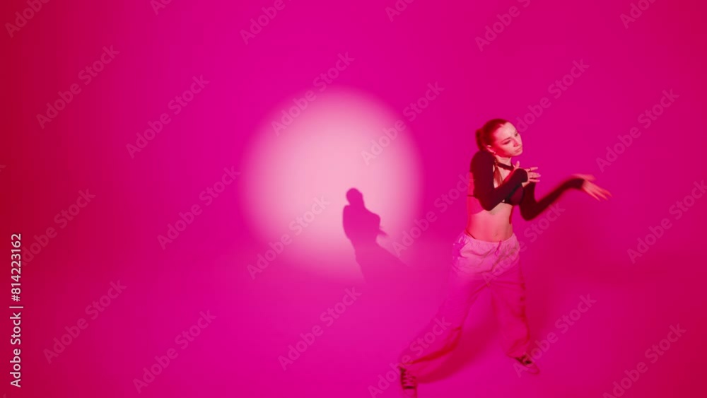 Brunette woman dancing moves rhythmically performing hip hop dance in round light spot with pink color strobe flashing lights in studio environment. Female dancer demonstrates modern choreography
