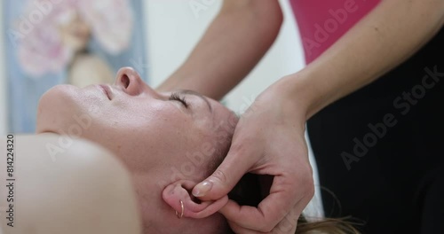 Ear massage face of relaxed young woman enjoying ear massage at beauty salon. hands of unrecognizable masseur massaging auricle of beautiful female client sitting on massage table at spa salon. photo