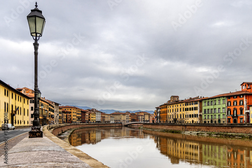 Travel scene of Pisa Italy with colorful houses and apartment buildings along  the Arno River. Copy space in the big sky.