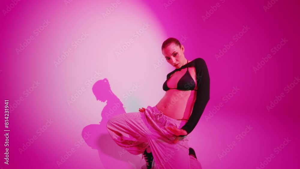 Sexy woman dancing performing hip hop dance in white light spot with pink color wall in studio. Handsome female dancer shows modern choreography making sudden aggressive movements, handheld wide shot Sexy woman dancing performing hip hop dance in white light spot with pink color wall in studio. Handsome female dancer shows modern choreography making sudden aggressive movements, handheld wide shot