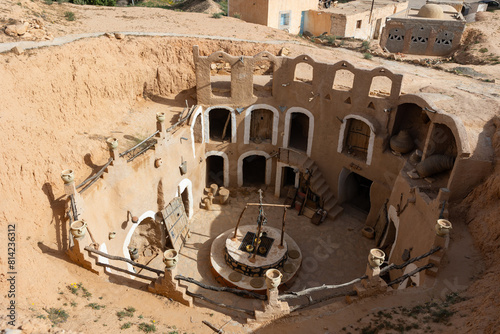 Traditional ancient Berber troglodyte underground dwellings in Tunisian town of Matmata with arched doorways carved into earth and communal well in courtyard photo