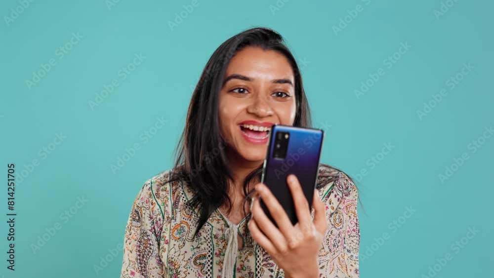 Smiling woman having friendly conversations during teleconference meeting using smartphone, studio background. Indian person having fun catching up with mates during online videocall, camera B Smiling woman having friendly conversations during teleconference meeting using smartphone, studio background. Indian person having fun catching up with mates during online videocall, camera B