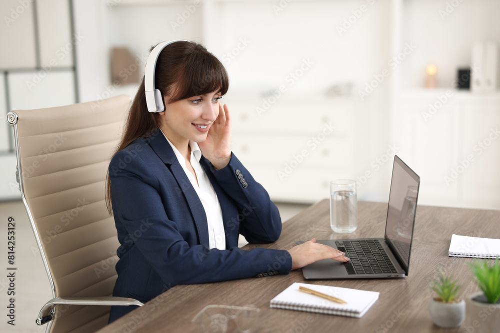 Woman in headphones watching webinar at wooden table in office Woman in headphones watching webinar at wooden table in office