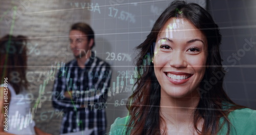Image of graphs and trading board, biracial smiling businesswoman with coworkers in background