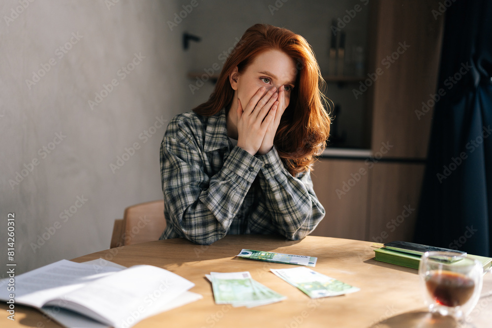 Desperate young woman counting money with sad expression, sitting at home kitchen table. Sad female having financial literacy and loan repayment. Concept of financial crisis. Desperate young woman counting money with sad expression, sitting at home kitchen table. Sad female having financial literacy and loan repayment. Concept of financial crisis.