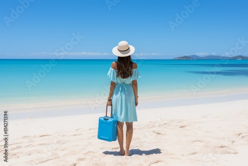 A woman in a flowing blue dress walks barefoot on a serene beach, with the ocean stretching into the horizon. The tranquil scene evokes a sense of peaceful escape and relaxation.