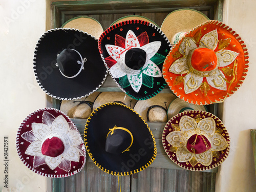 Six Mexican charros hats of several colors hanging on a wall