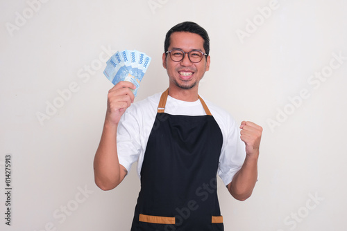 A man wearing apron clenched fist showing excited while holding money