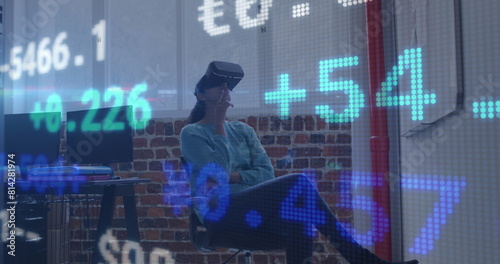 Image of trading board over caucasian woman sitting on chair and using vr headset in office