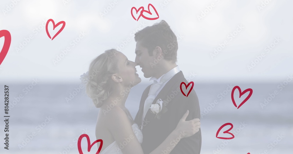 Fototapeta premium Caucasian couple wearing wedding attire, kissing on beach