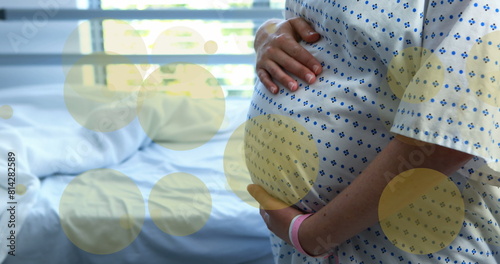 Image of green spots over biracial pregnant woman touching her stomach in hospital