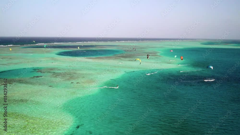Kitesurfers gliding over a vibrant coral reef on a sunny day, aerial view Kitesurfers gliding over a vibrant coral reef on a sunny day, aerial view