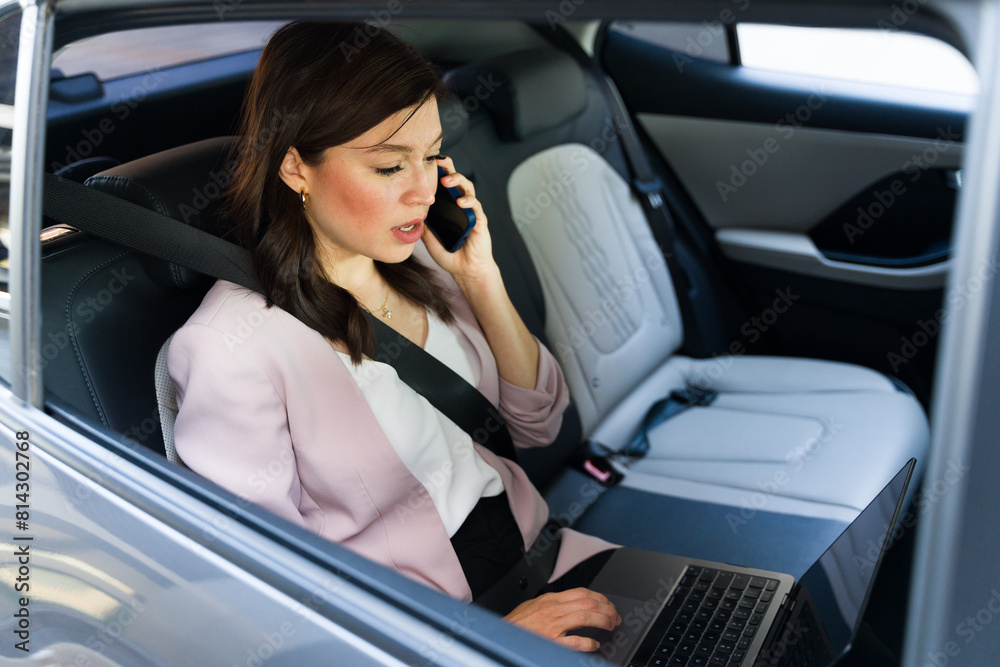 Professional and busy woman multitasking on laptop and smartphone during car commute Professional and busy woman multitasking on laptop and smartphone during car commute