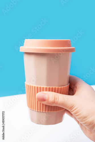 Female hand hold ceramic glass with coffee on blue and white background, side view.