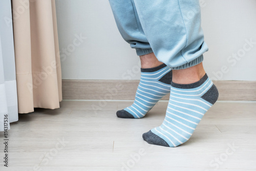 Male legs in blue socks stand on tiptoes against the background of wall, home workout concept.