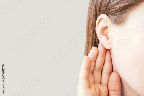 Woman listens attentively with her palm to her ear close-up on a gray background.
