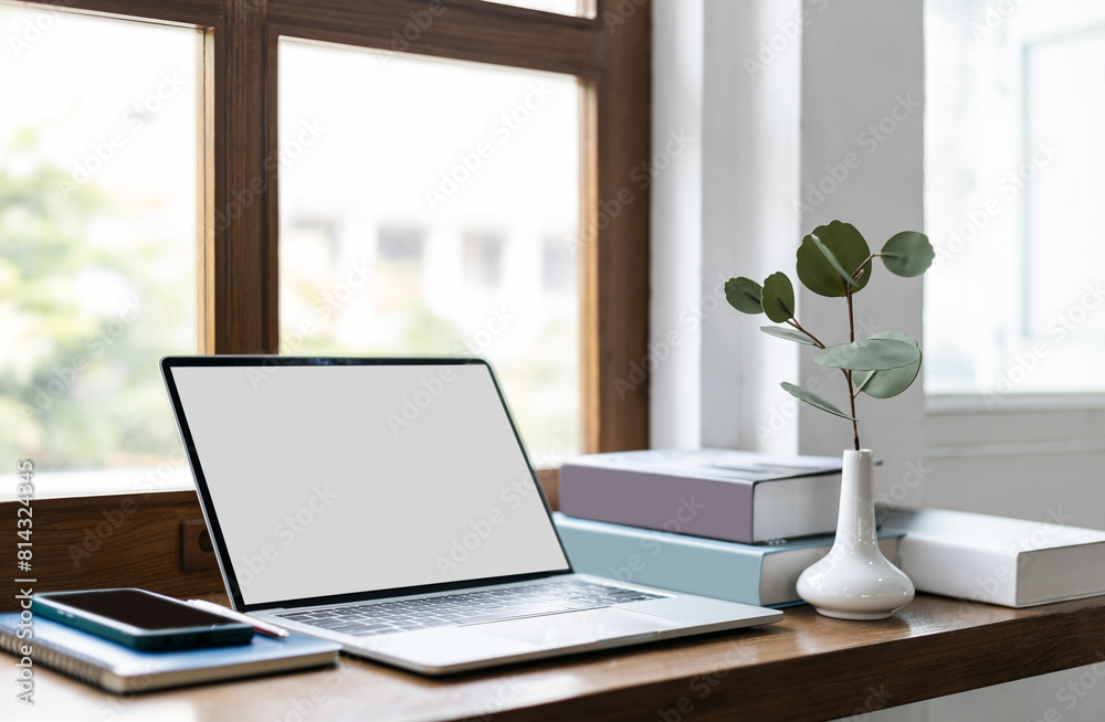 Fototapeta premium Comfortable workplace on wooden counter by the window and laptop, smart phone, note book and pen. vase with small tree inside and a book for read