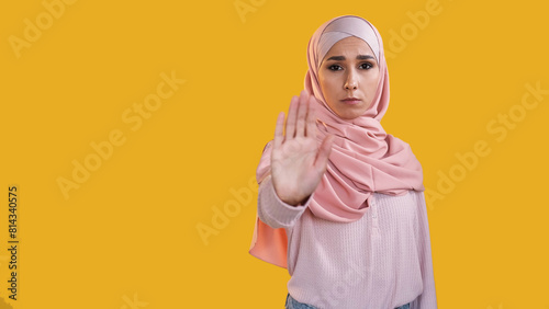 Enough gesture. Female protest. Concerned dissatisfied frowning woman in hijab warning with outstretched hand palm isolated on orange empty space background. © golubovy