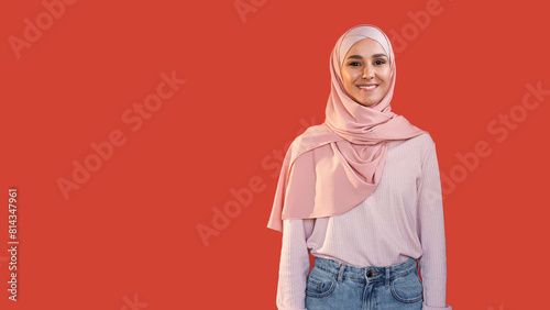 Happy woman. Modest beauty. Positive emotion. Portrait of pleased optimistic smiling girl in hijab isolated on red empty space background.