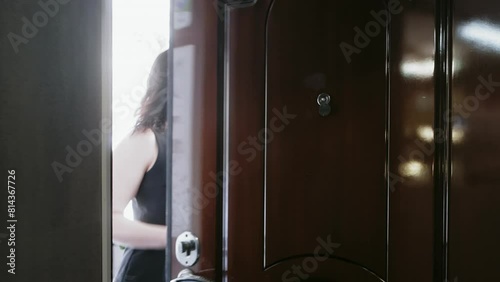 Rear view of woman opening door and taking exit. Female is wearing sleeveless dress while leaving on sunnyn day. Black door in dark room. 
