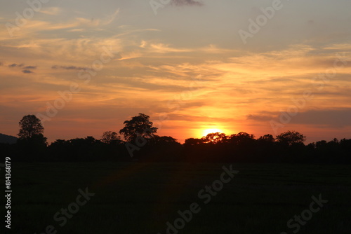 Natural Sunset Sunrise Over Field Or Meadow. Bright Dramatic Sky And Dark Ground. Countryside Landscape Under Scenic Colorful Sky At Sunset Dawn Sunrise. Sun Over Skyline, Horizon. Warm Colours.