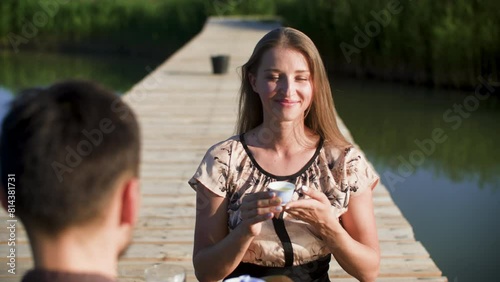 Happy woman drinking Oolong tea with man. Couple is sitting on wooden pier amidst lake. They are enjoying ceremony during sunny day.
