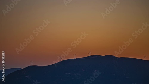 Silhouette of wind turbines generating energy on top of mountain, distance time lapse view photo