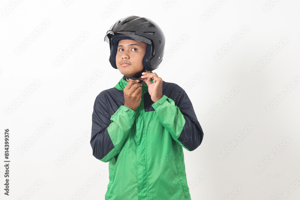 Portrait of Asian online taxi driver wearing green jacket and helmet demonstrating how to wear helmet correctly. Isolated image on white background Portrait of Asian online taxi driver wearing green jacket and helmet demonstrating how to wear helmet correctly. Isolated image on white background