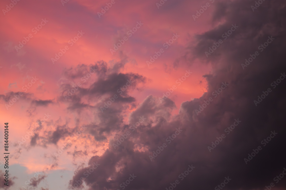 A stormy dramatic sky is filled with clouds that are bathed in hues of pink and purple from the setting sun. Contrasting colors create a moody and atmospheric scene with dark, ominous cloud formations