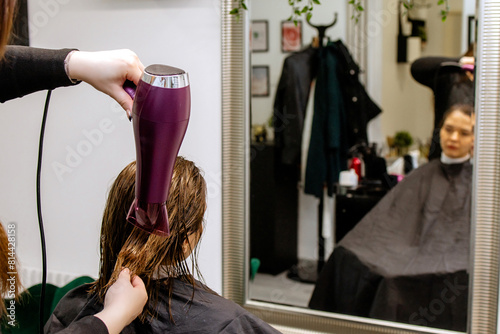 Woman professional hairdresser doing hair styling to client in beauty salon, stylist doing hair care procedures, drying hair with hairdryer to client