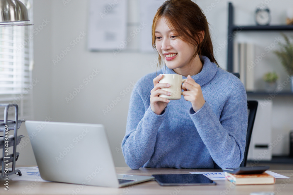 Freelancer asian woman working from home and using laptop sitting in living room with cup of hot coffee enjoying Freelancer asian woman working from home and using laptop sitting in living room with cup of hot coffee enjoying