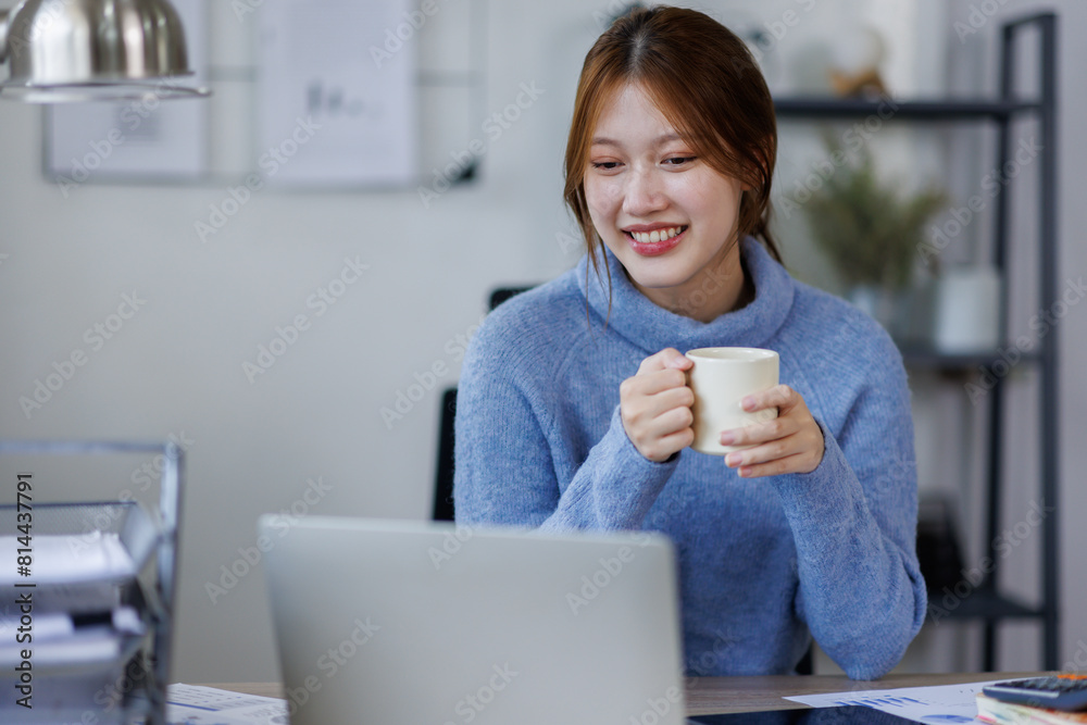 Freelancer asian woman working from home and using laptop sitting in living room with cup of hot coffee enjoying Freelancer asian woman working from home and using laptop sitting in living room with cup of hot coffee enjoying