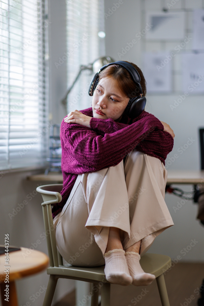 Brunette young asian woman listening music while resting on couch at home relaxing with headphones