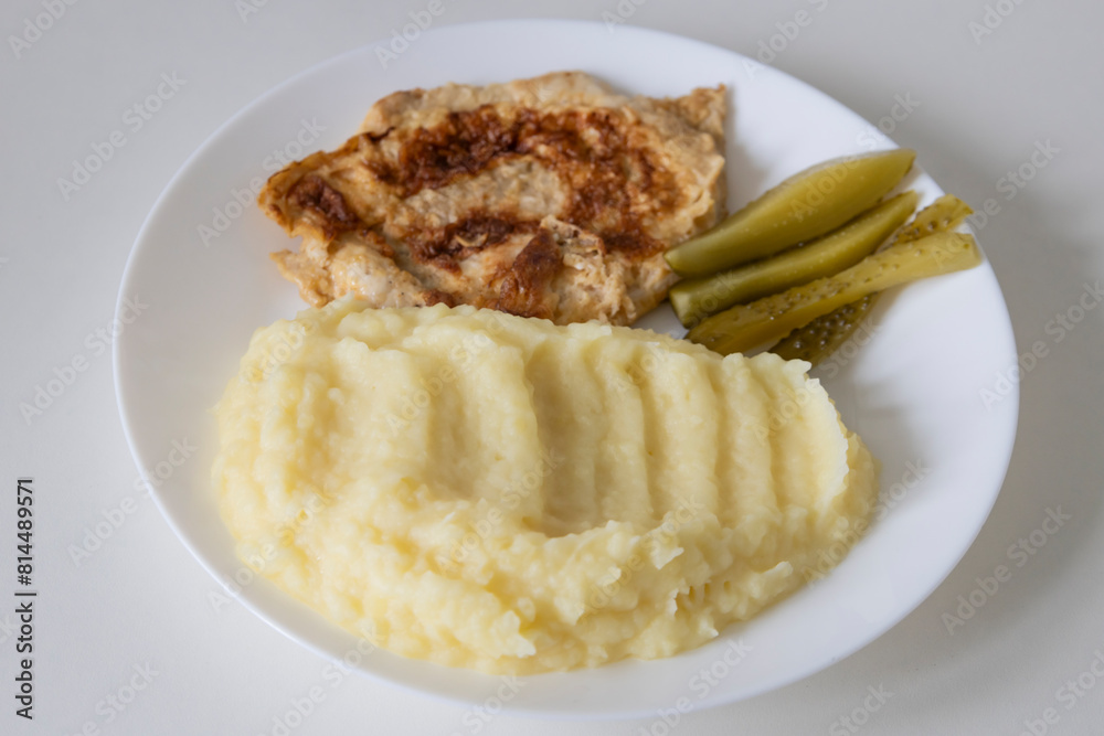 A delicious breakfast or lunch with mashed potatoes, chop with pickled cucumbers on the white plate. A delicious breakfast or lunch with mashed potatoes, chop with pickled cucumbers on the white plate.
