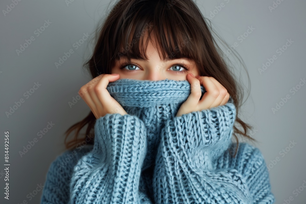 A girl pulls a jumper over her face. Girl's beautiful eyes look through the jumper and hat. Concept of warmth and coldness A girl pulls a jumper over her face. Girl's beautiful eyes look through the jumper and hat. Concept of warmth and coldness