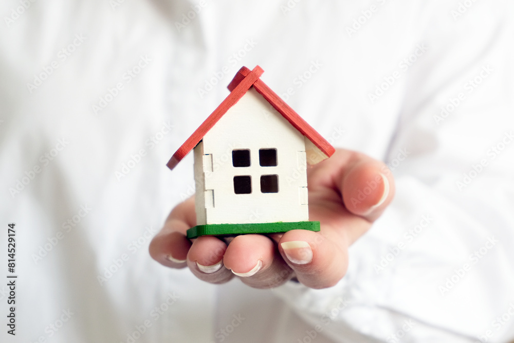 A woman dressed in a white shirt holds a small house in front of her A woman dressed in a white shirt holds a small house in front of her