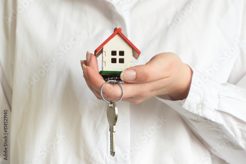 A woman dressed in a white shirt holds a small house and a key in front of her